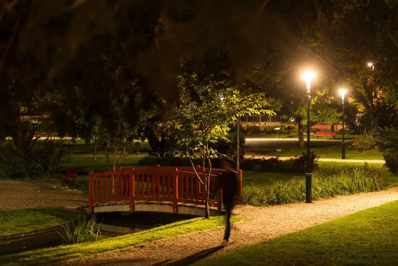 Allée de parc la nuit, piéton sous un candélabre à détection SensyCity