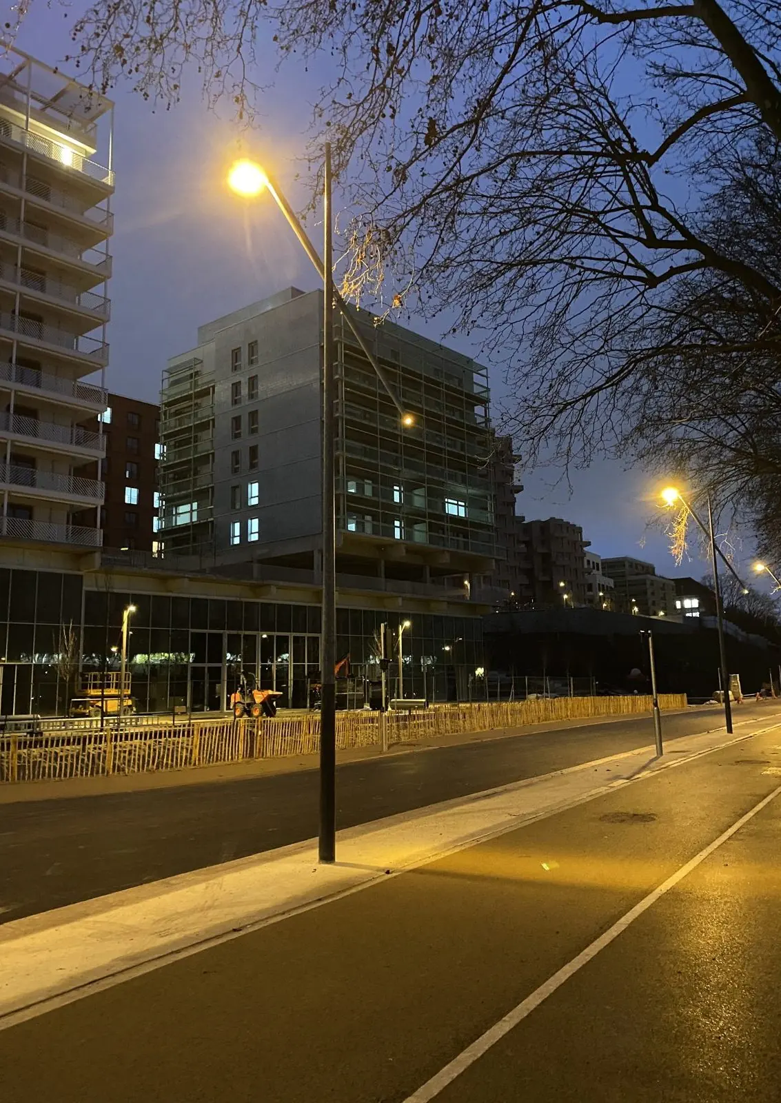 Rue du Village des Athlètes à la tombée de la nuit, éclairée par des mâts réemployés