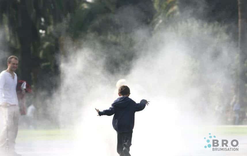 Enfant courant dans la brume d'une aire de jeux BRO, parent en arrière-plan