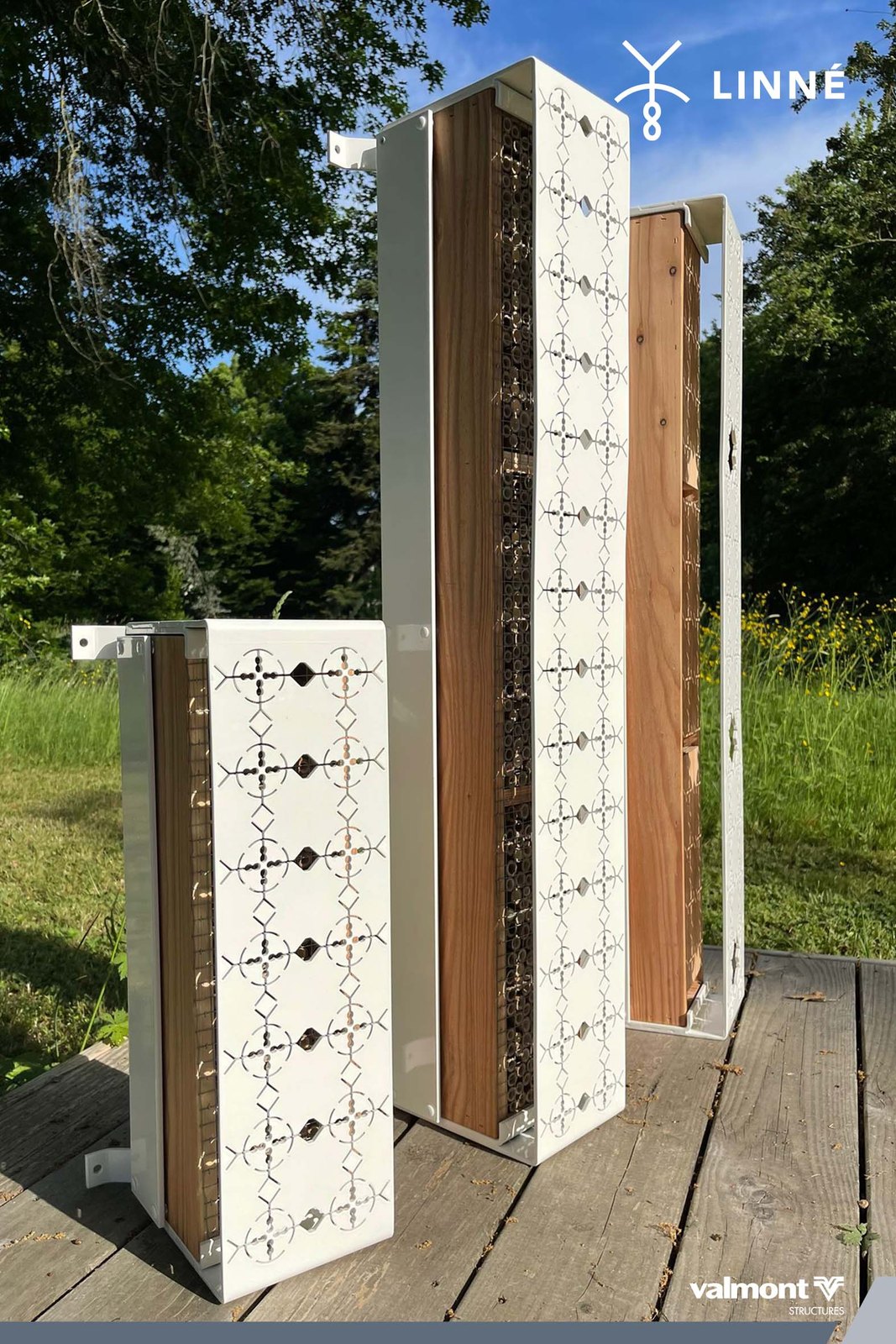 Trois totems de biodiversité en deux tailles, bois et dentelle d'aluminium, posés sur une terrasse